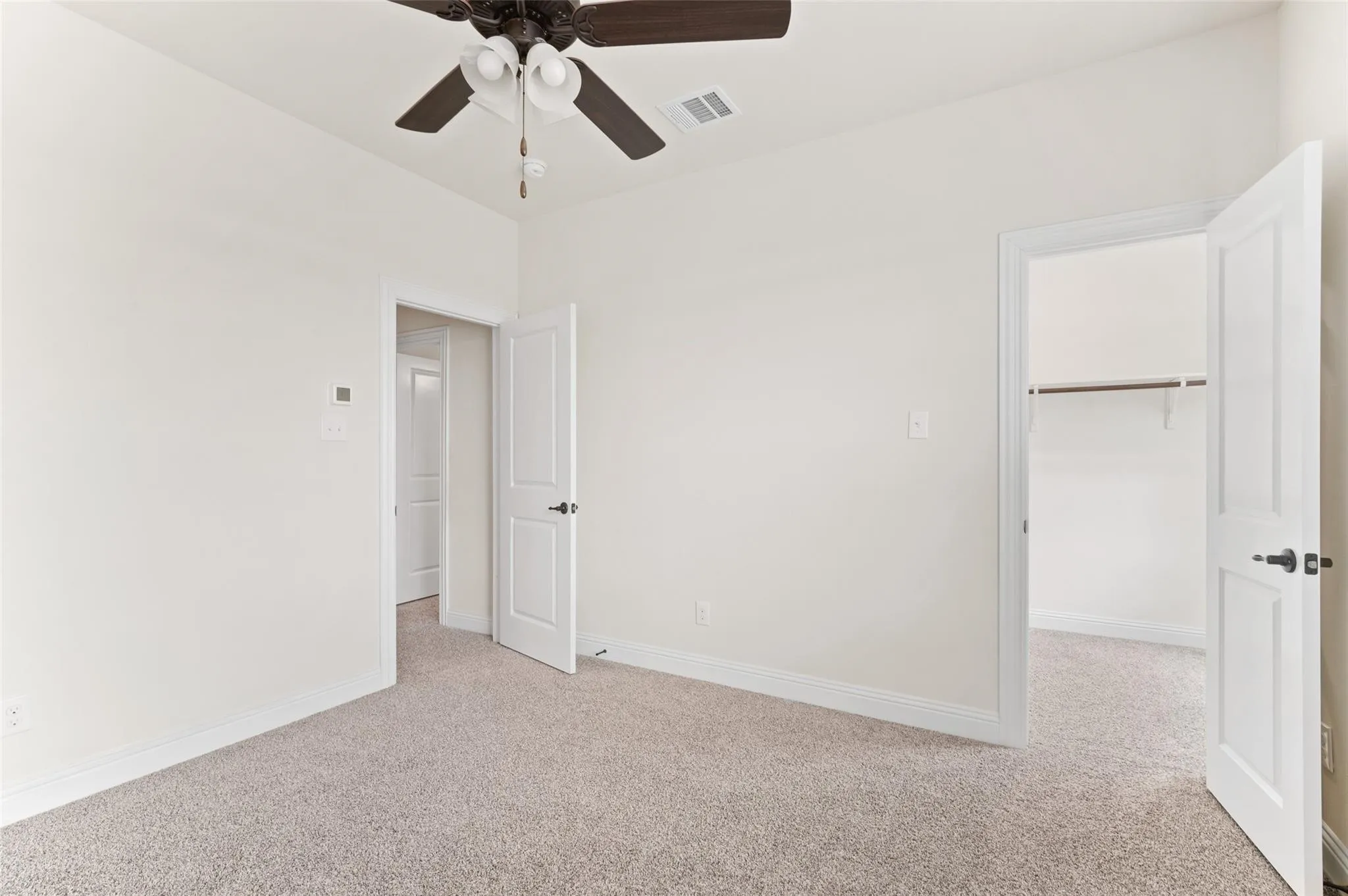 Neutral wall finishes, light-toned carpeting, ceiling fan with integrated lighting, two-panel interior doors with dark hardware, and a closet with a built-in shelf and hanging rod