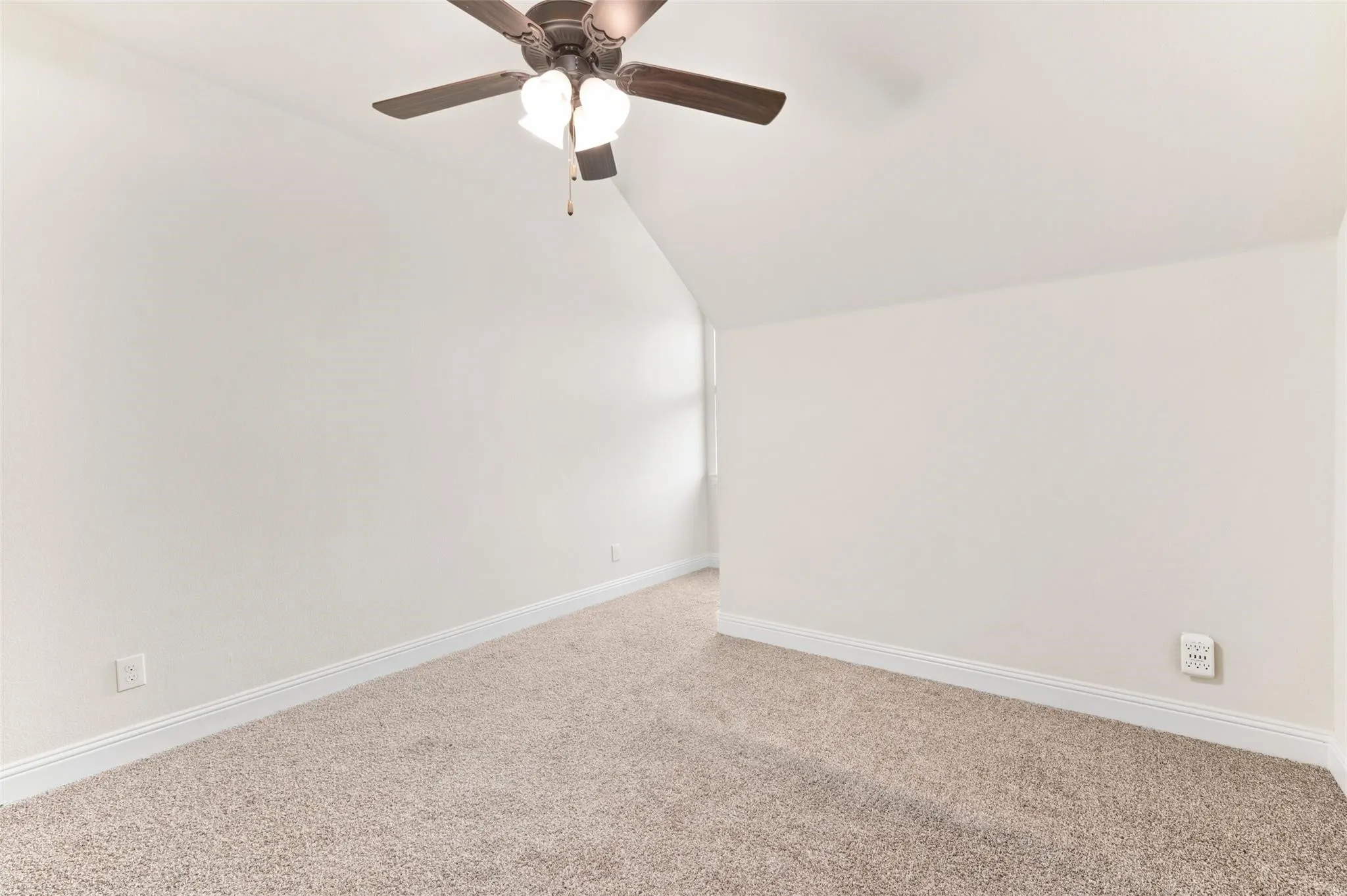 Sloped ceiling room featuring a ceiling fan with light fixture and neutral carpet flooring