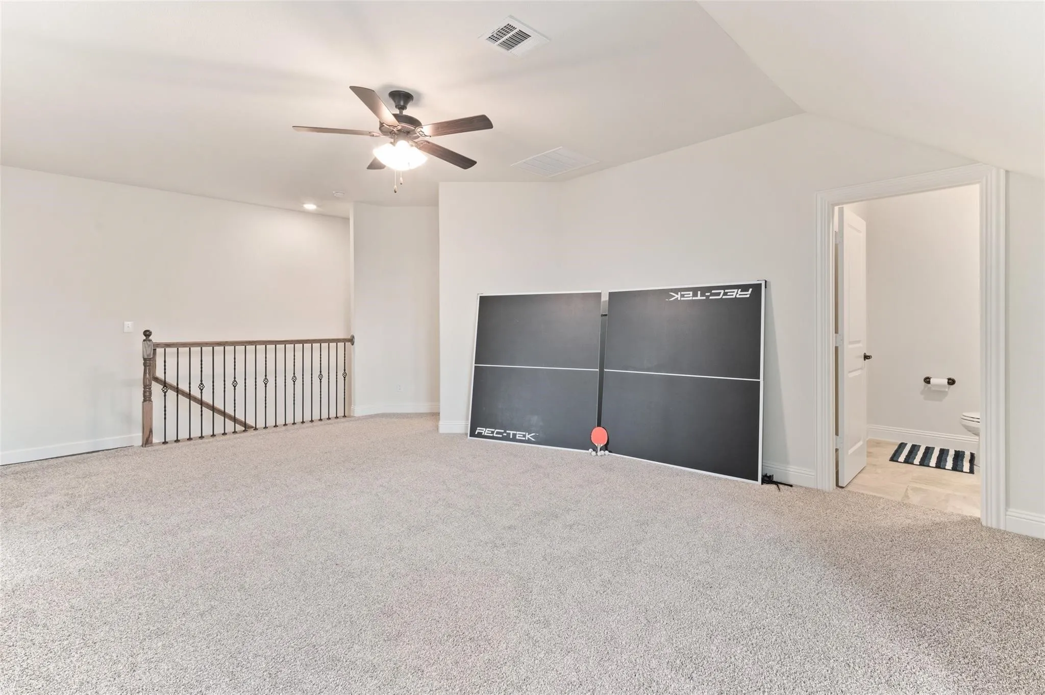Spacious carpeted room featuring a ceiling fan with light, recessed lighting, and an open doorway to a tiled bathroom with a toilet