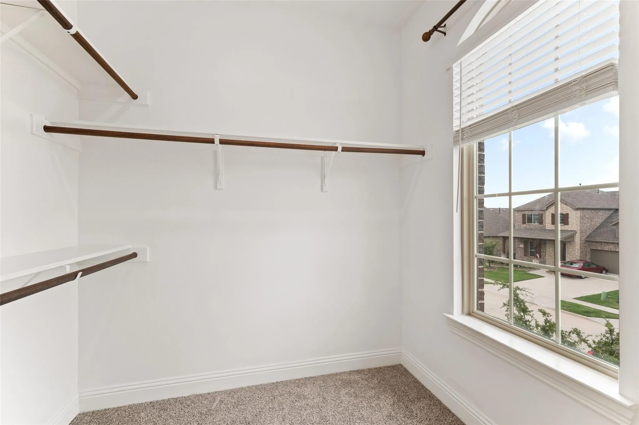 Built-in shelving and hanging rods, window with horizontal blinds, neutral carpeting
