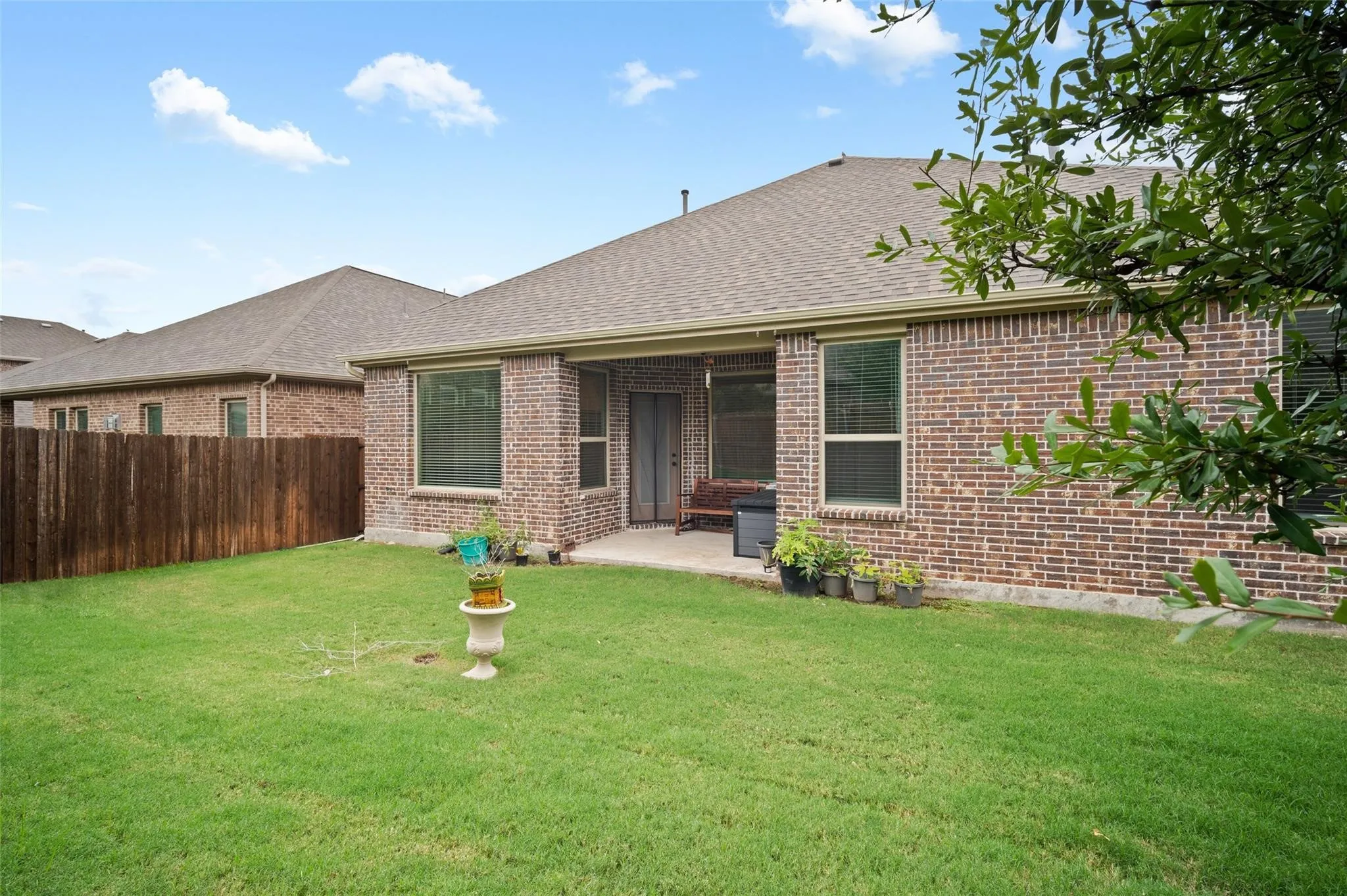 Expansive grassy yard with a brick exterior, covered patio, and a wood privacy fence