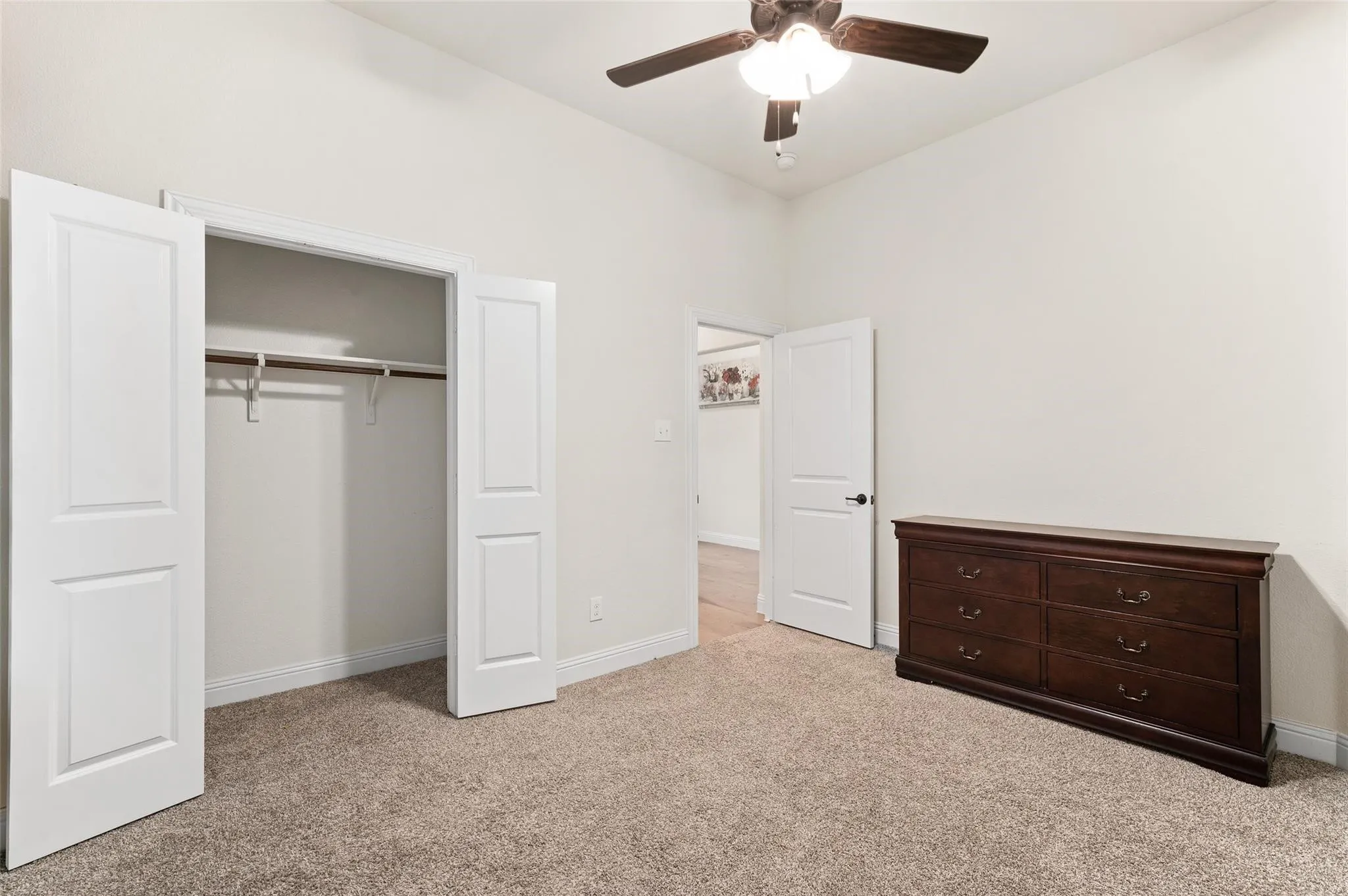 Carpeted room featuring a ceiling fan with integrated lighting and a built-in closet with double doors and a hanging rod
