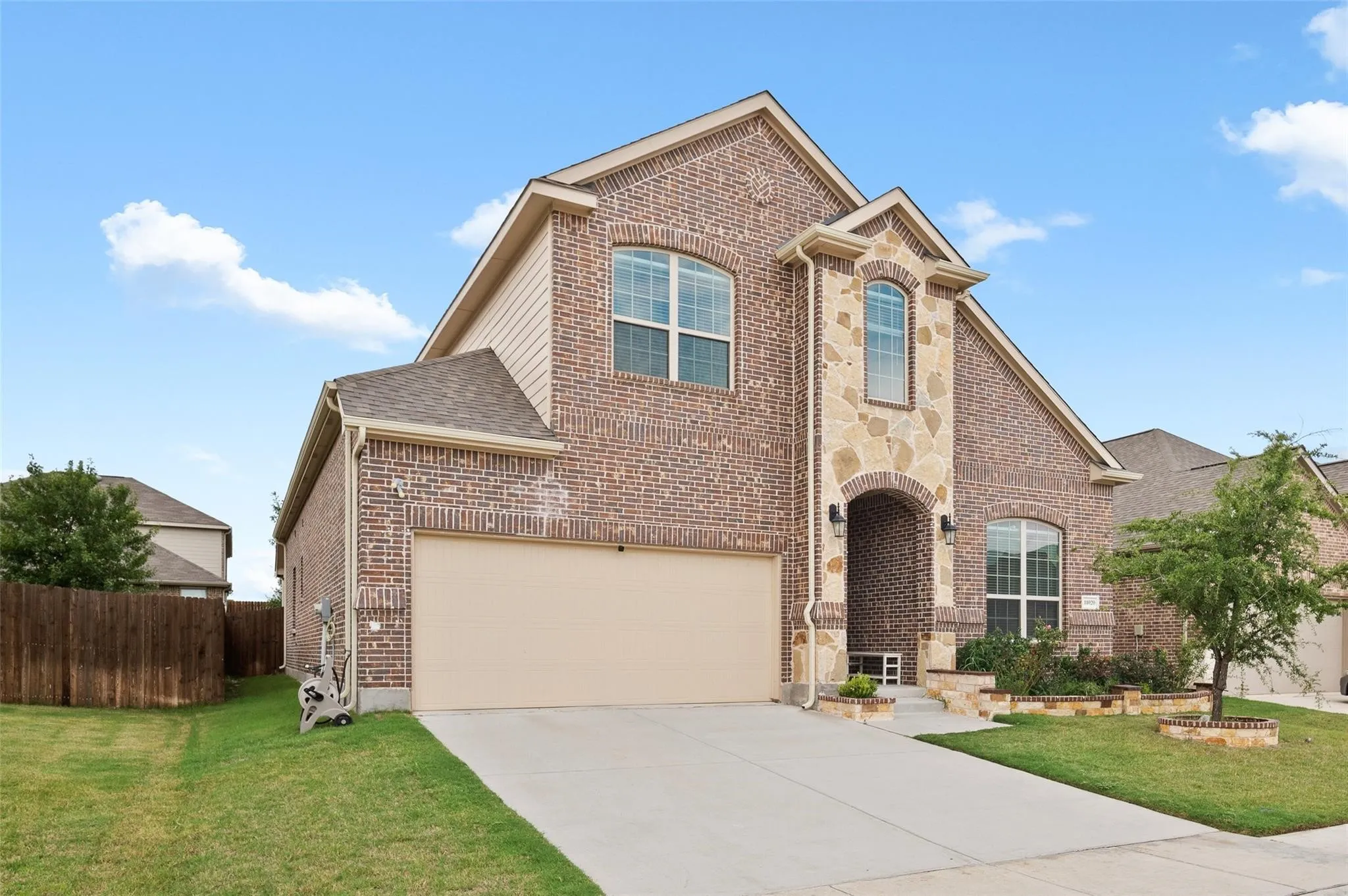 Brick and stone exterior with an arched entryway, attached two-car garage, and established landscaping