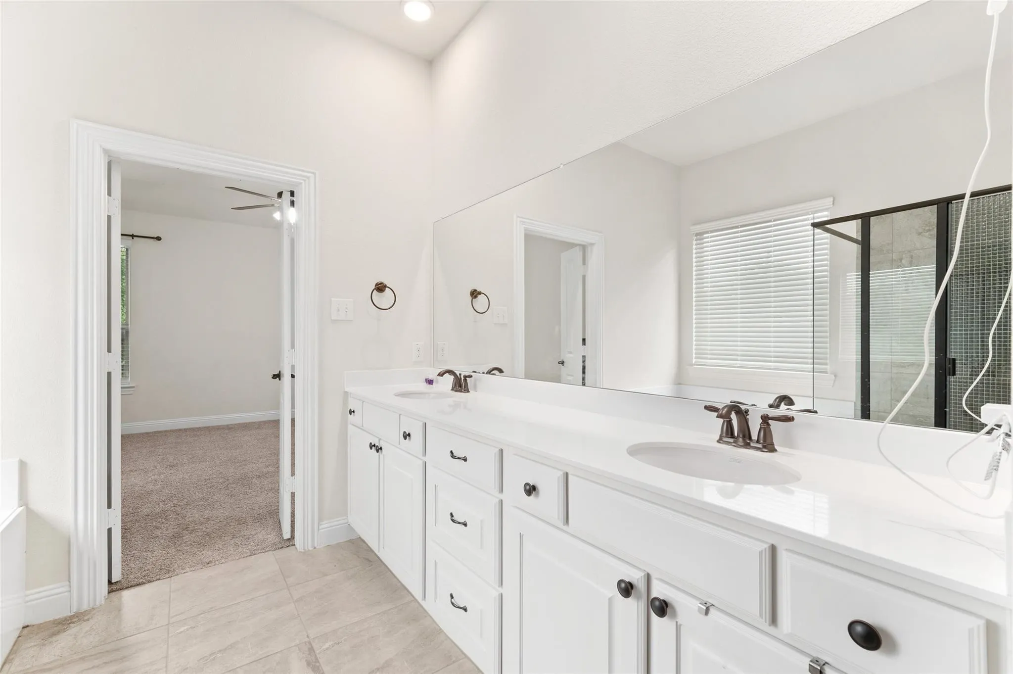 Double vanity with white cabinetry, integrated sinks, white countertops, and bronze-finish fixtures