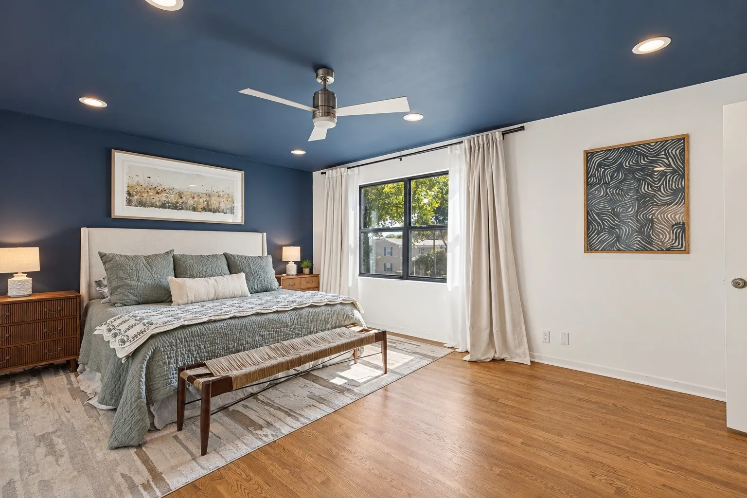 Hardwood flooring, recessed lighting, ceiling fan, dark accent wall, and a large window with drapes