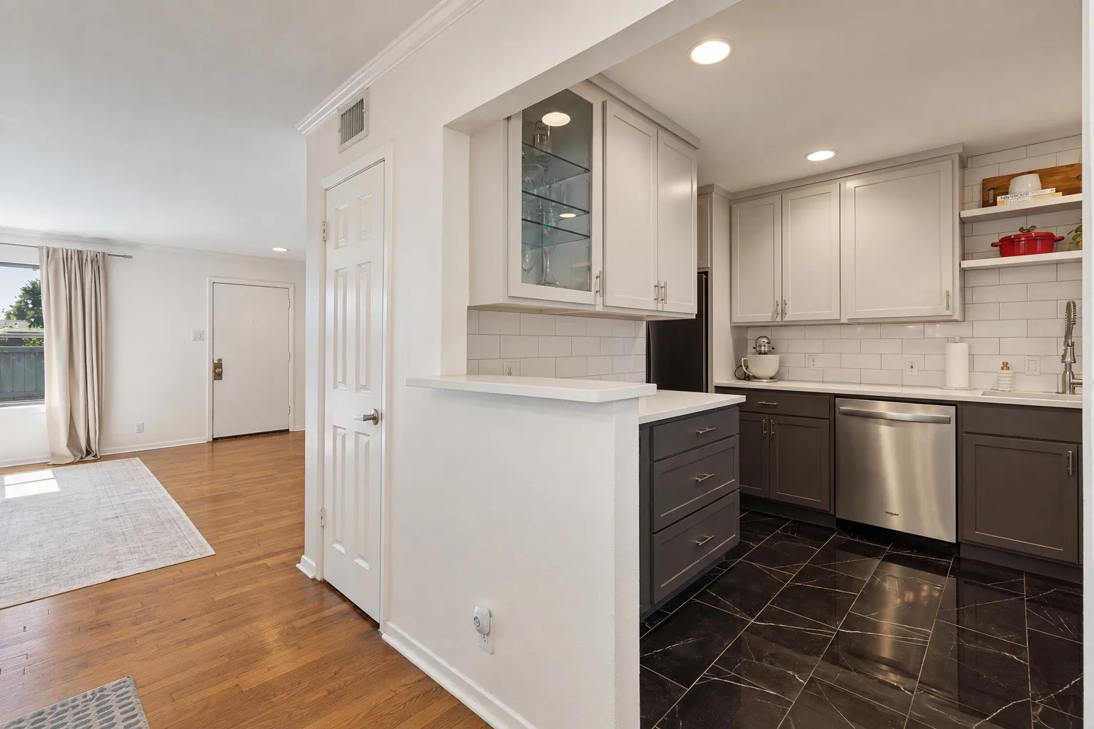 Kitchen featuring two-tone cabinetry, stainless steel dishwasher, white subway tile backsplash, and dark tile flooring