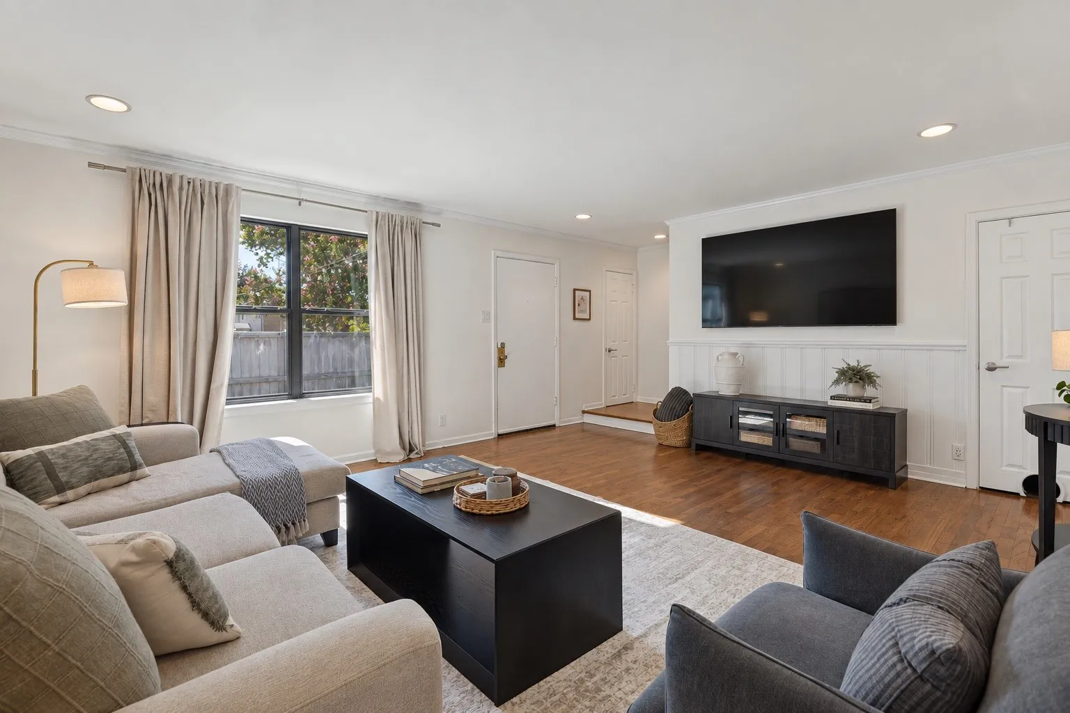 Recessed lighting, wood-finish flooring, white paneled accent wall, and a large window