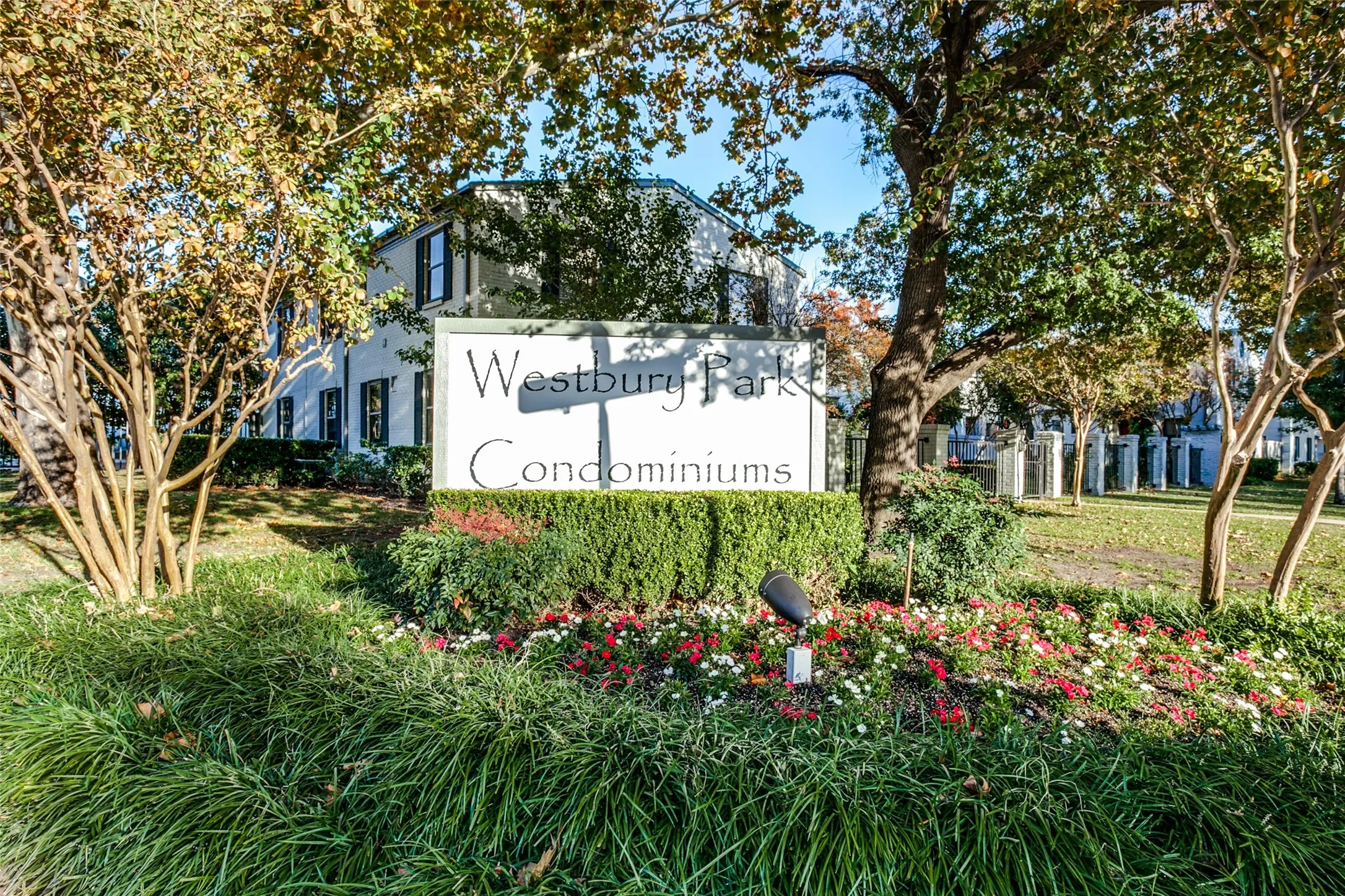 Entry monument with lush landscaping, mature trees, and building exteriors