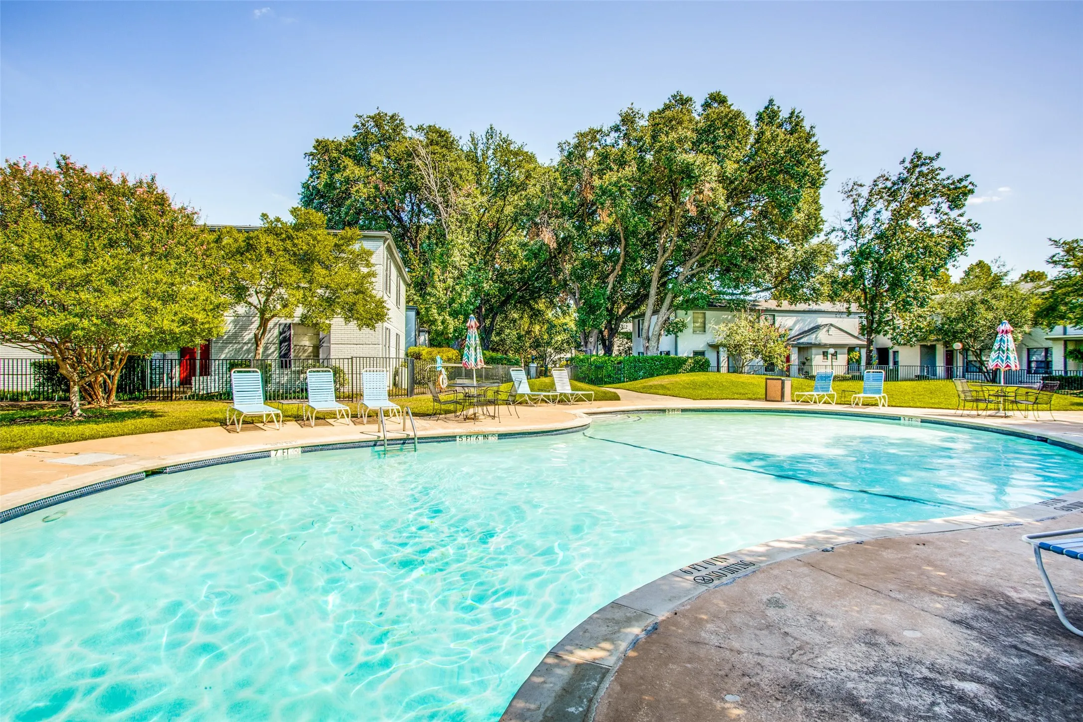 Outdoor swimming pool with a concrete surround, surrounded by mature trees and manicured lawns