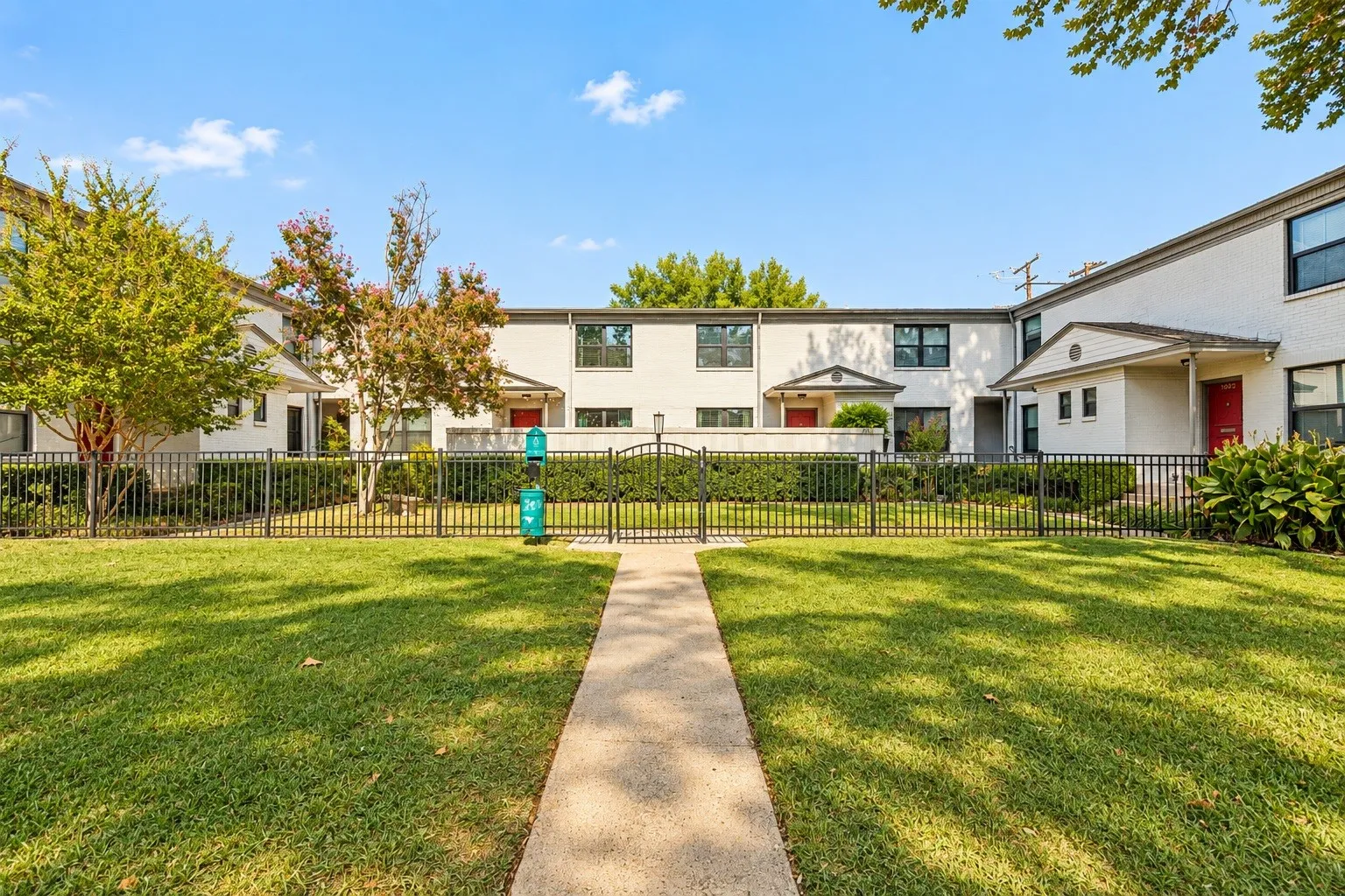 White brick exterior, black windows, red entry doors, black metal fencing, and green landscaping