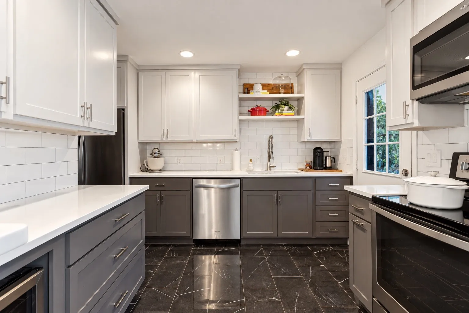 Two-tone cabinetry with white upper cabinets and gray lower cabinets, white subway tile backsplash, stainless steel appliances, white countertops, and dark tile flooring
