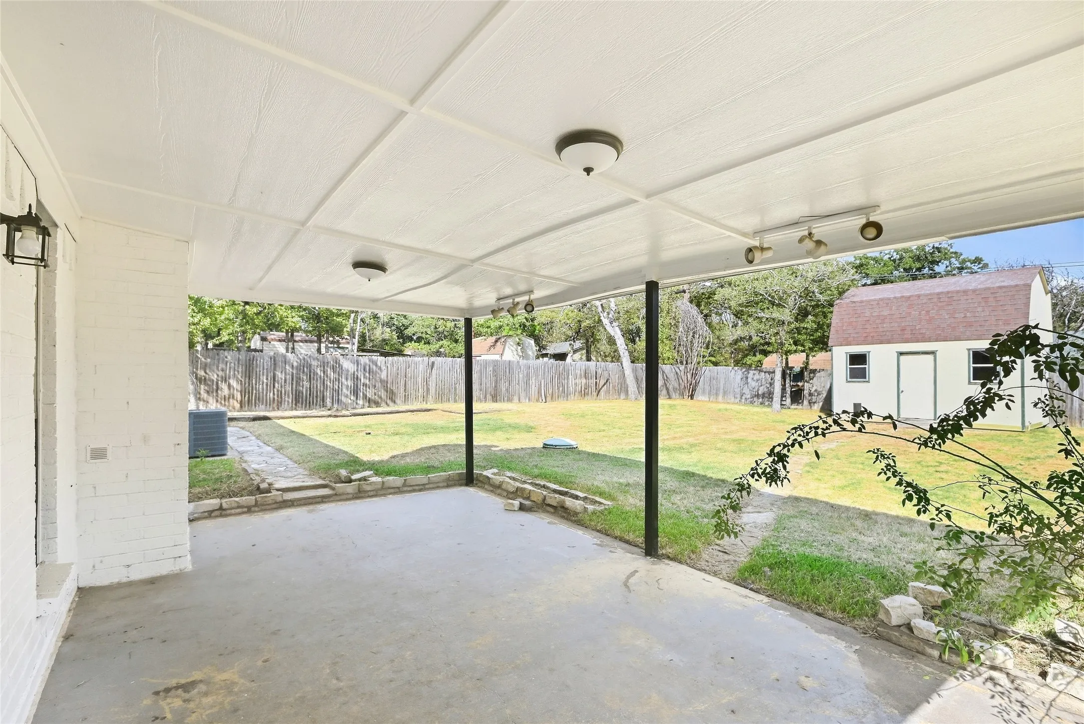 Covered concrete patio with overhead lighting, a spacious grass yard, and a detached storage shed
