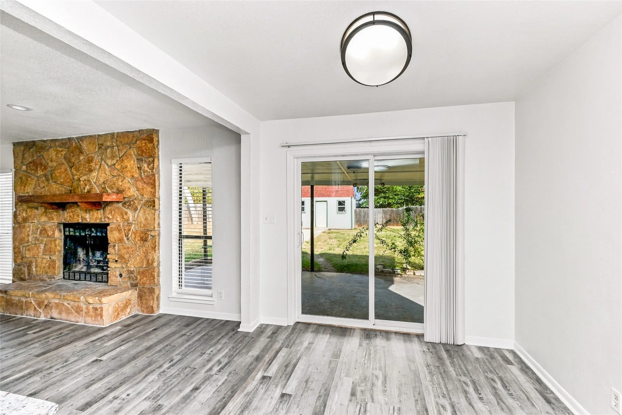 Stacked stone fireplace with a wood mantel, wood-finish flooring, recessed lighting, and sliding glass door to exterior