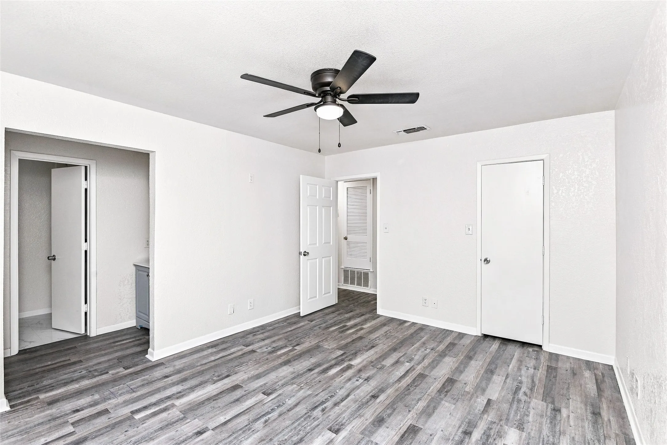 Expansive room featuring wood-finish flooring, a ceiling fan with integrated lighting, and multiple paneled doors