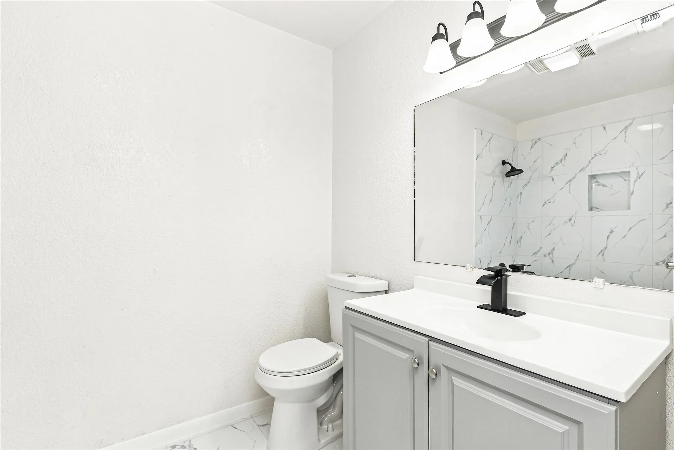 Bathroom featuring a light gray vanity, white countertop, black faucet, and white tiled shower with a niche