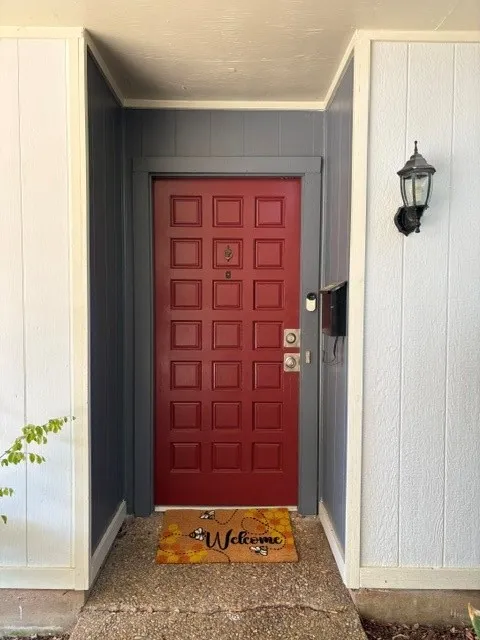 Red paneled entry door, exterior wall lantern, and textured white and gray siding