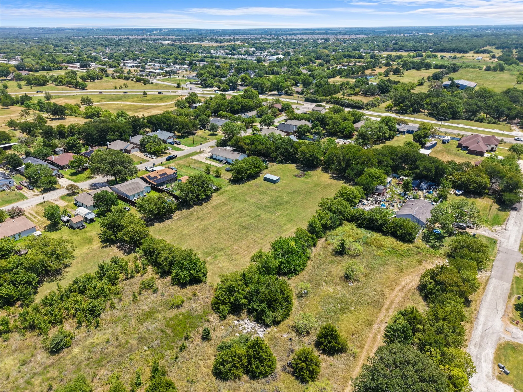 Expansive property featuring a large open field, surrounding residential structures, and mature trees