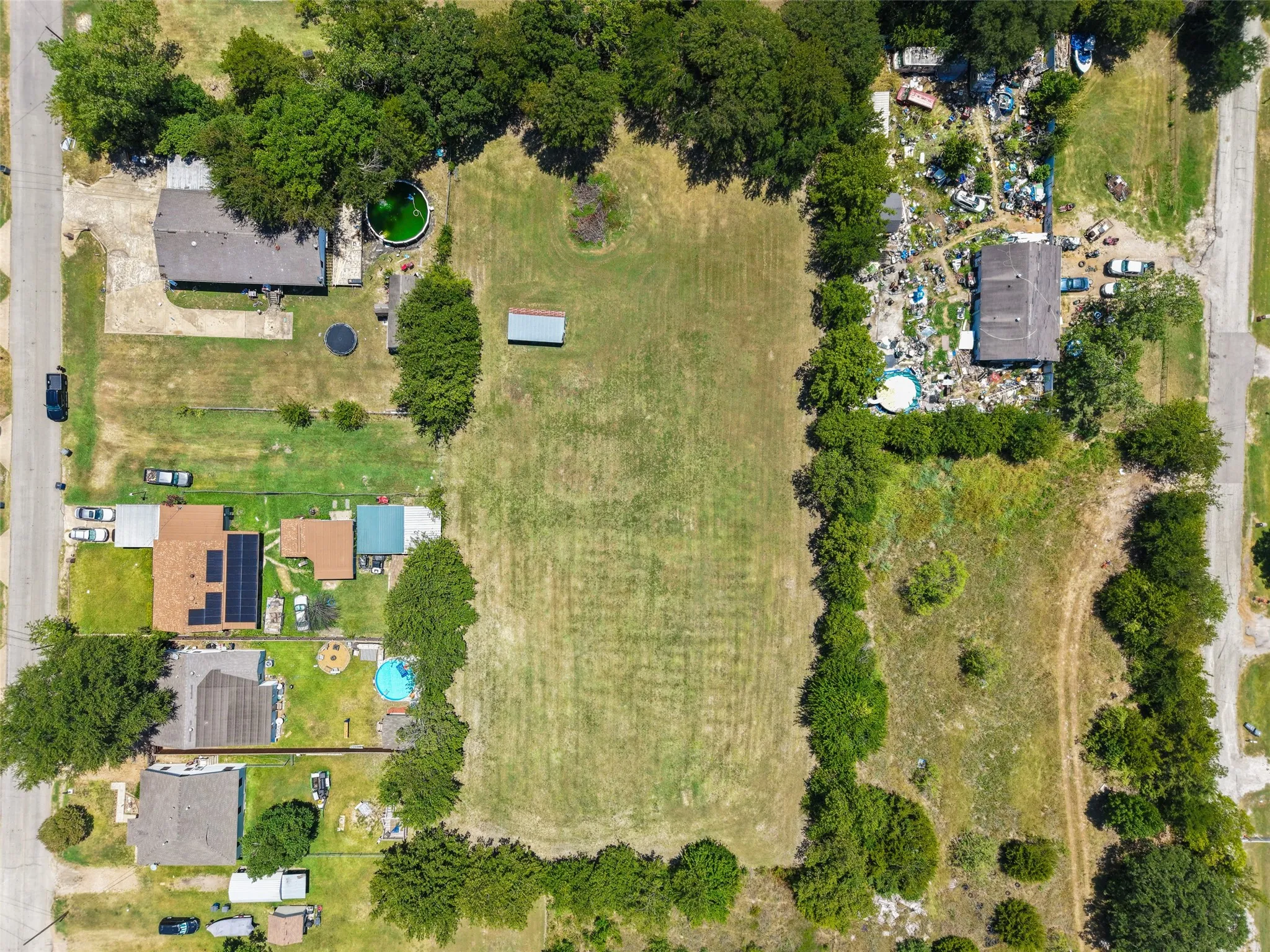 Expansive lot with cleared land, bordered by mature trees and residential properties
