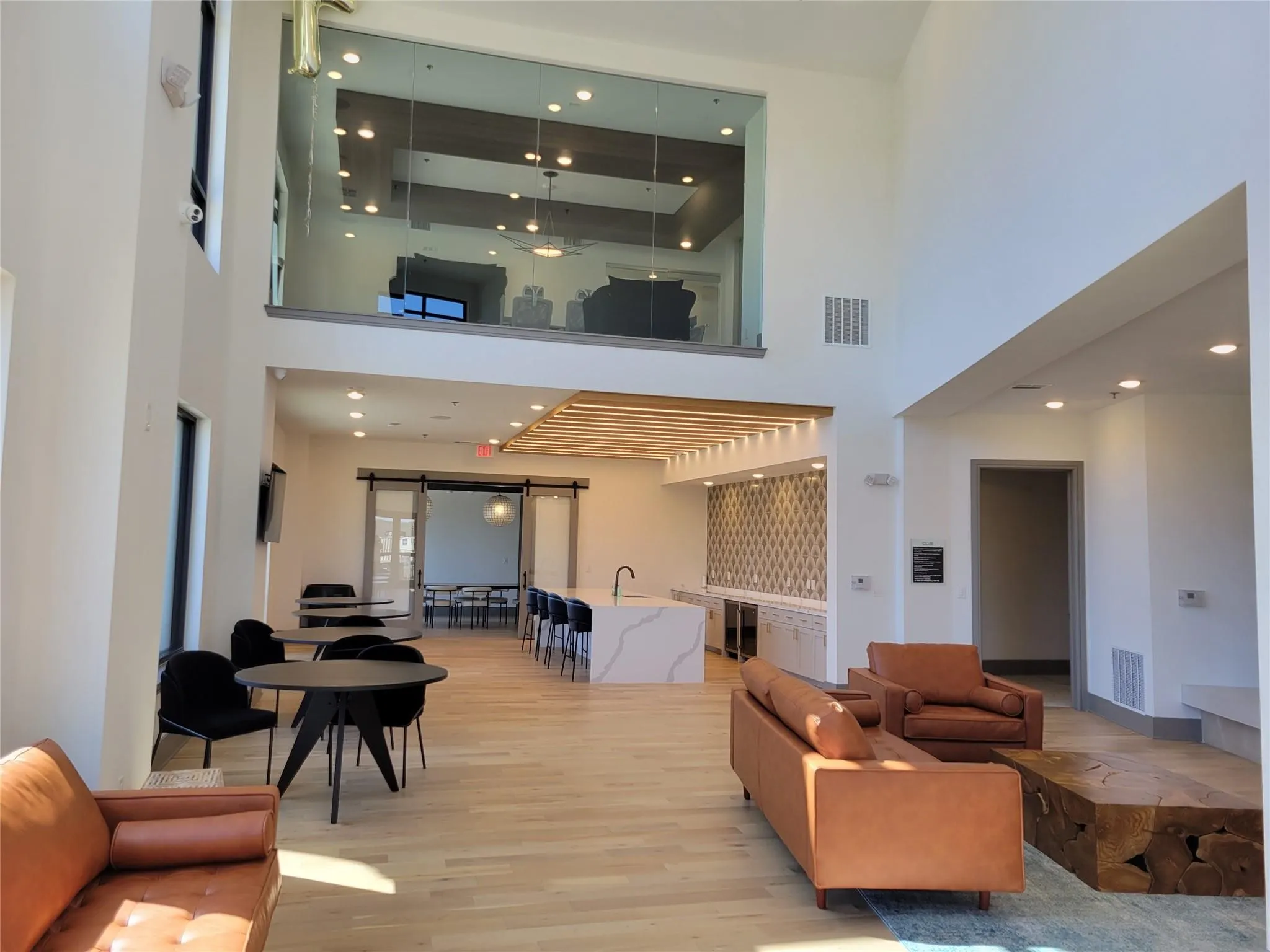 Double-height ceiling with an upper-level glass partition, wood-finish flooring, a central island with a waterfall edge, and sliding barn doors