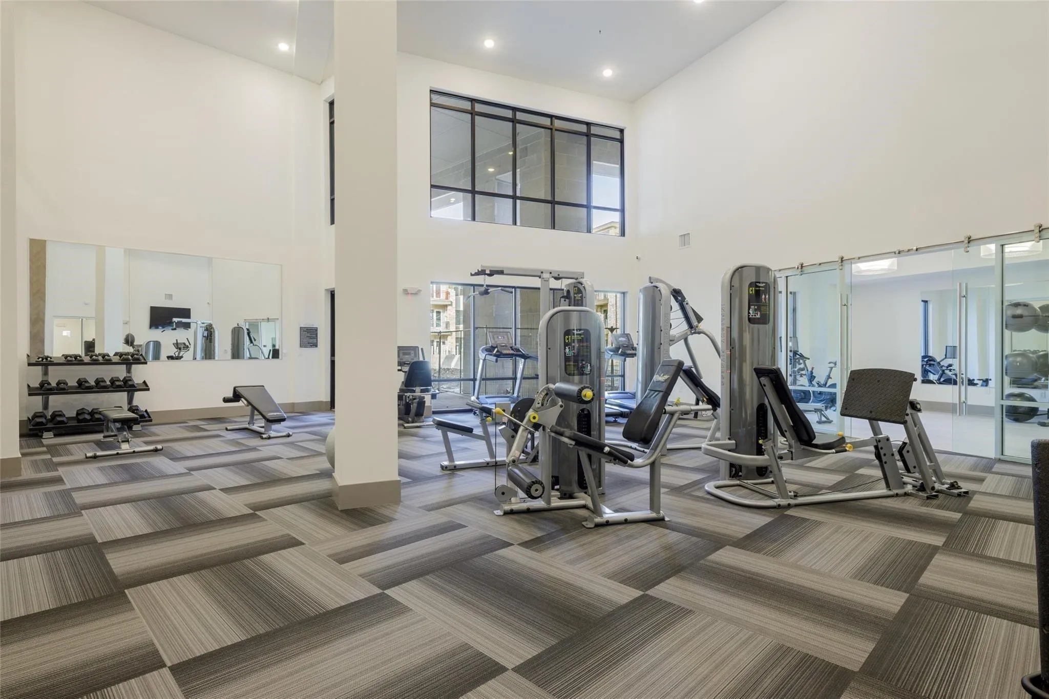 Fitness center featuring high ceilings, patterned carpet tile flooring, extensive exercise equipment, large wall-mounted mirrors, and transom windows