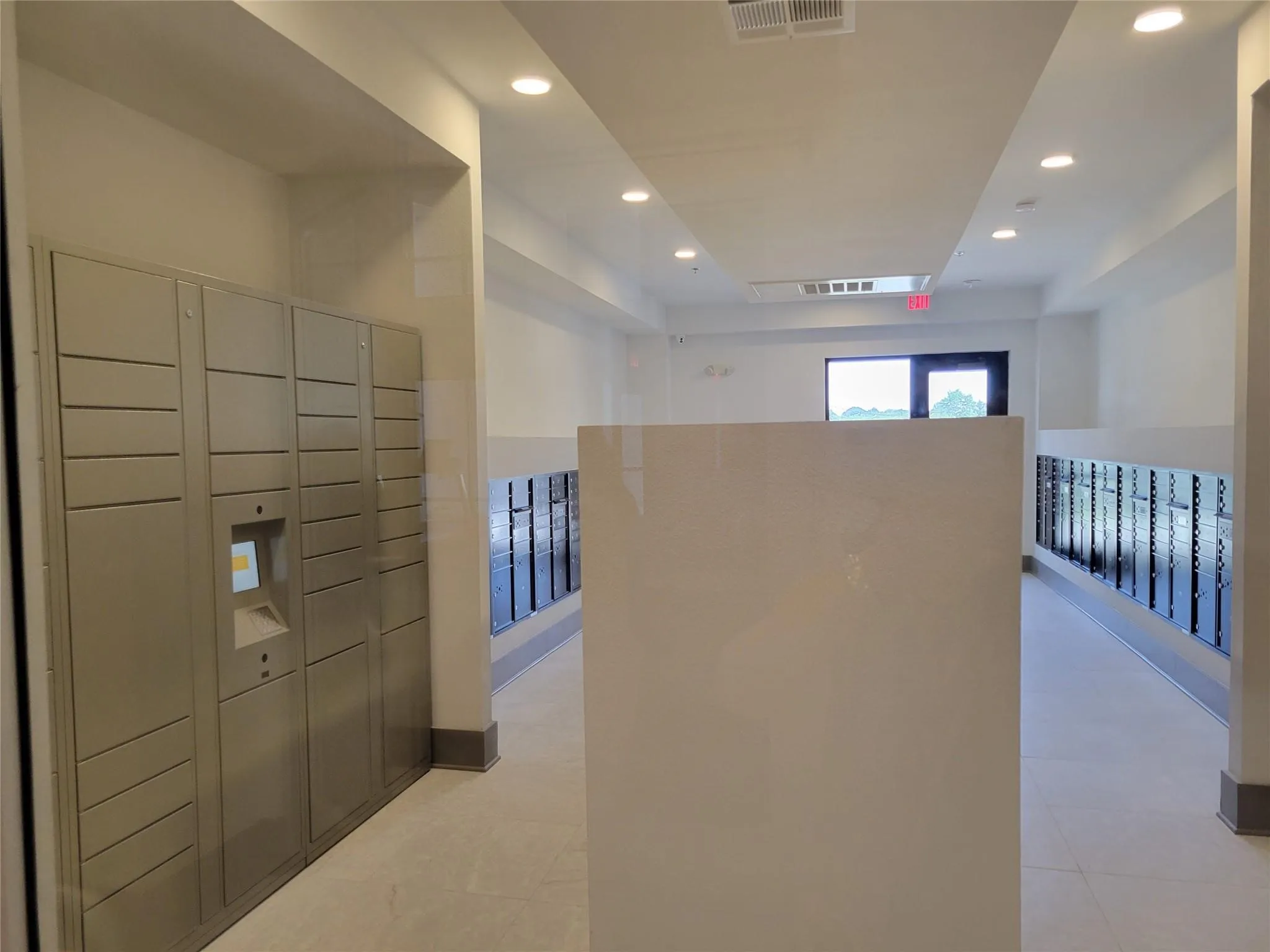 Secure parcel lockers and individual mailboxes within a brightly lit corridor featuring recessed lighting and a window providing natural light
