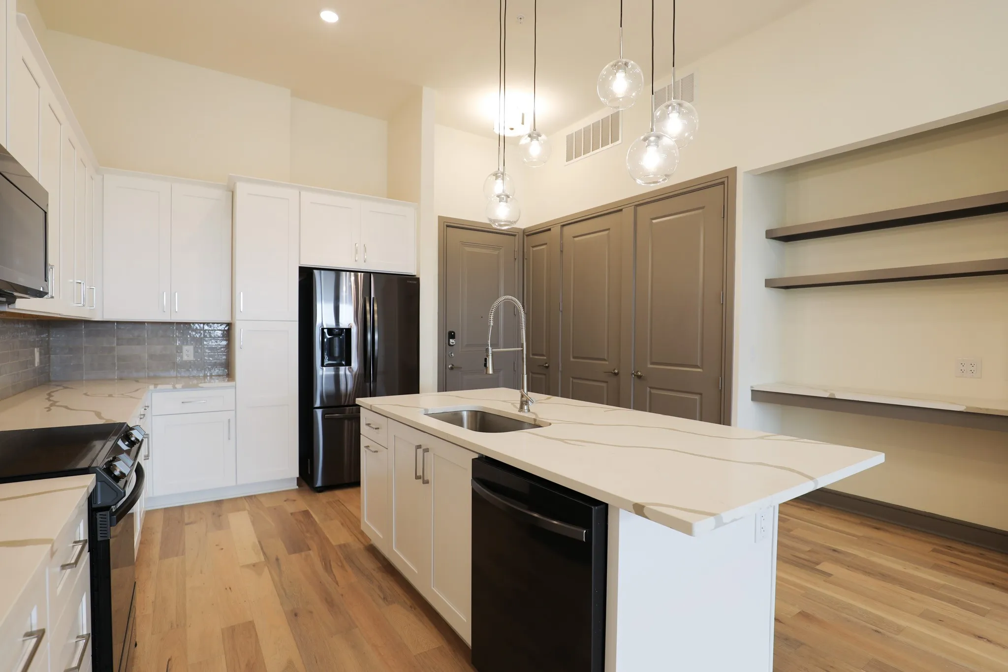 Gourmet kitchen featuring white shaker cabinetry, an expansive island with a waterfall countertop, pendant lighting, and wood-finish flooring