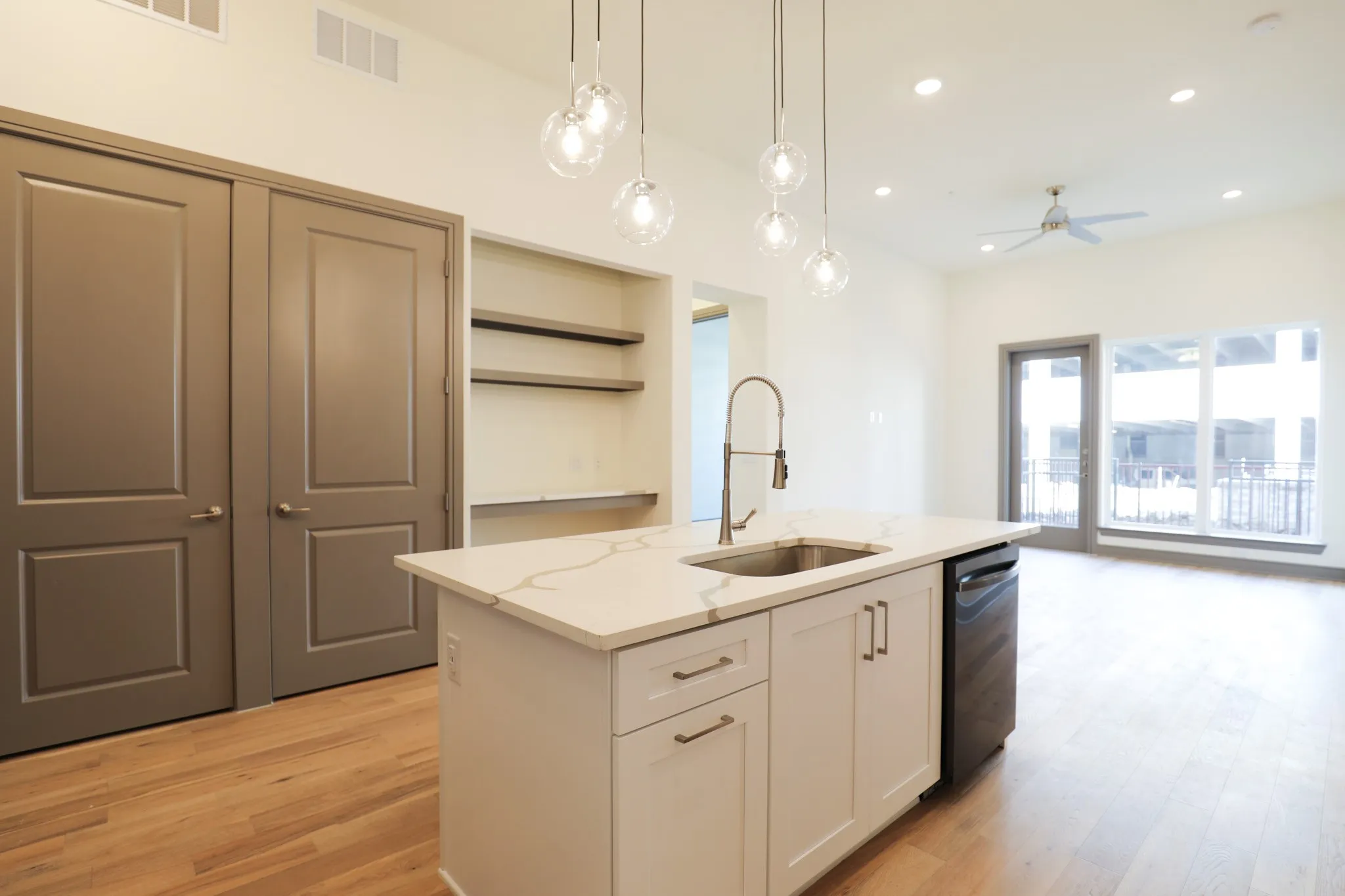 Open concept design with wood-finish flooring, a kitchen island featuring a sink and dishwasher, built-in shelving, and a ceiling fan