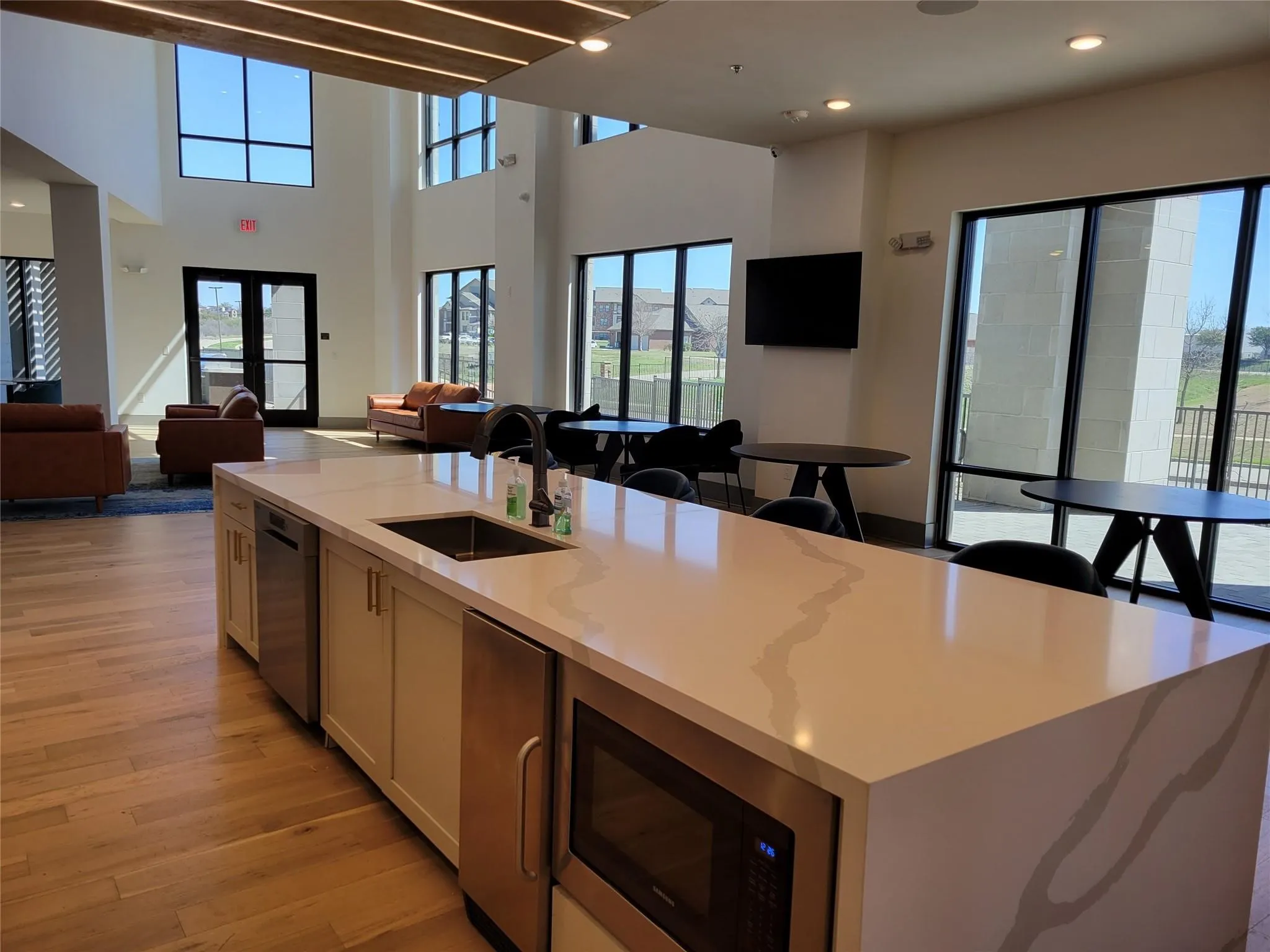 Open-concept communal area featuring high ceilings, wood-finish flooring, a kitchen island with integrated stainless steel appliances, and large windows