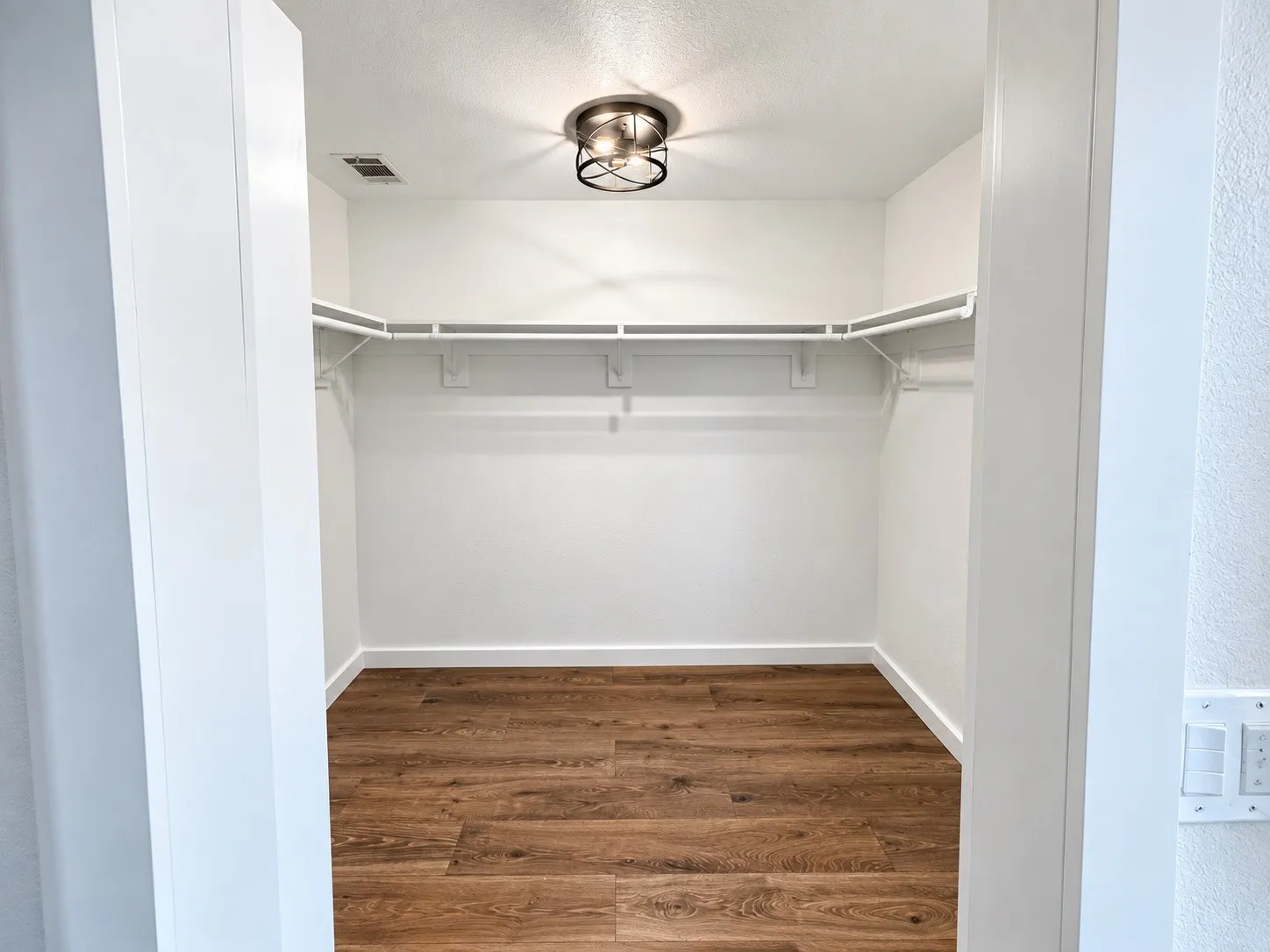 Walk-in closet with wood-finish flooring, white walls, built-in wire shelving, and a flush-mount light fixture