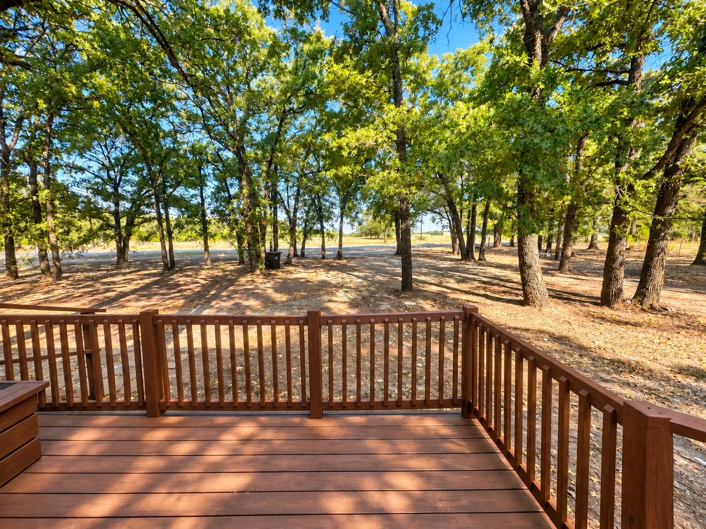 Spacious wooden deck with slatted railing, surrounded by mature trees