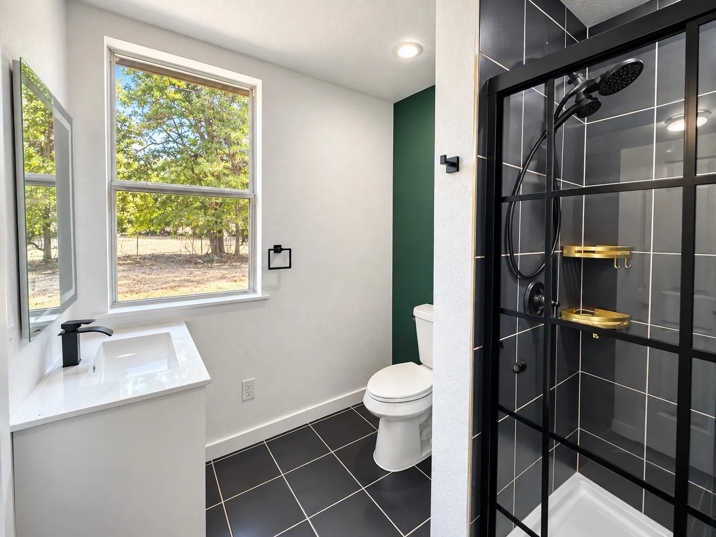 Modern bathroom featuring a single vanity with a white countertop, black tile flooring, a walk-in shower with black grid-patterned glass, and dark gray wall tiles