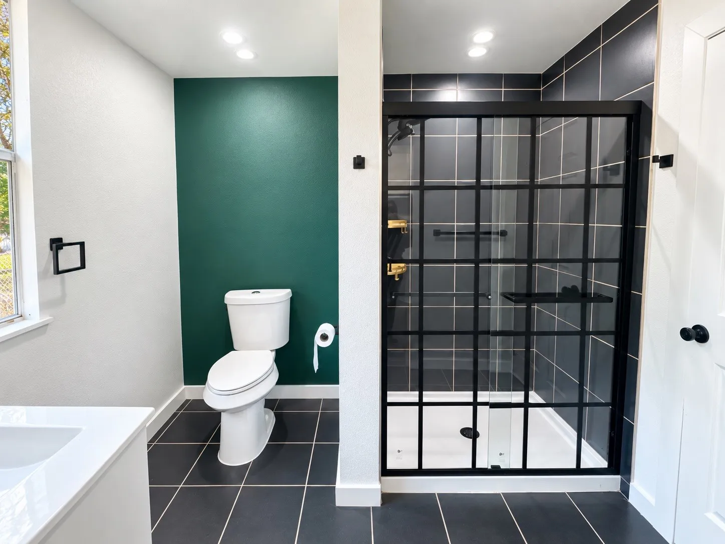 Modern bathroom featuring a black-framed glass shower enclosure, dark tile flooring, and a white vanity with an integrated sink