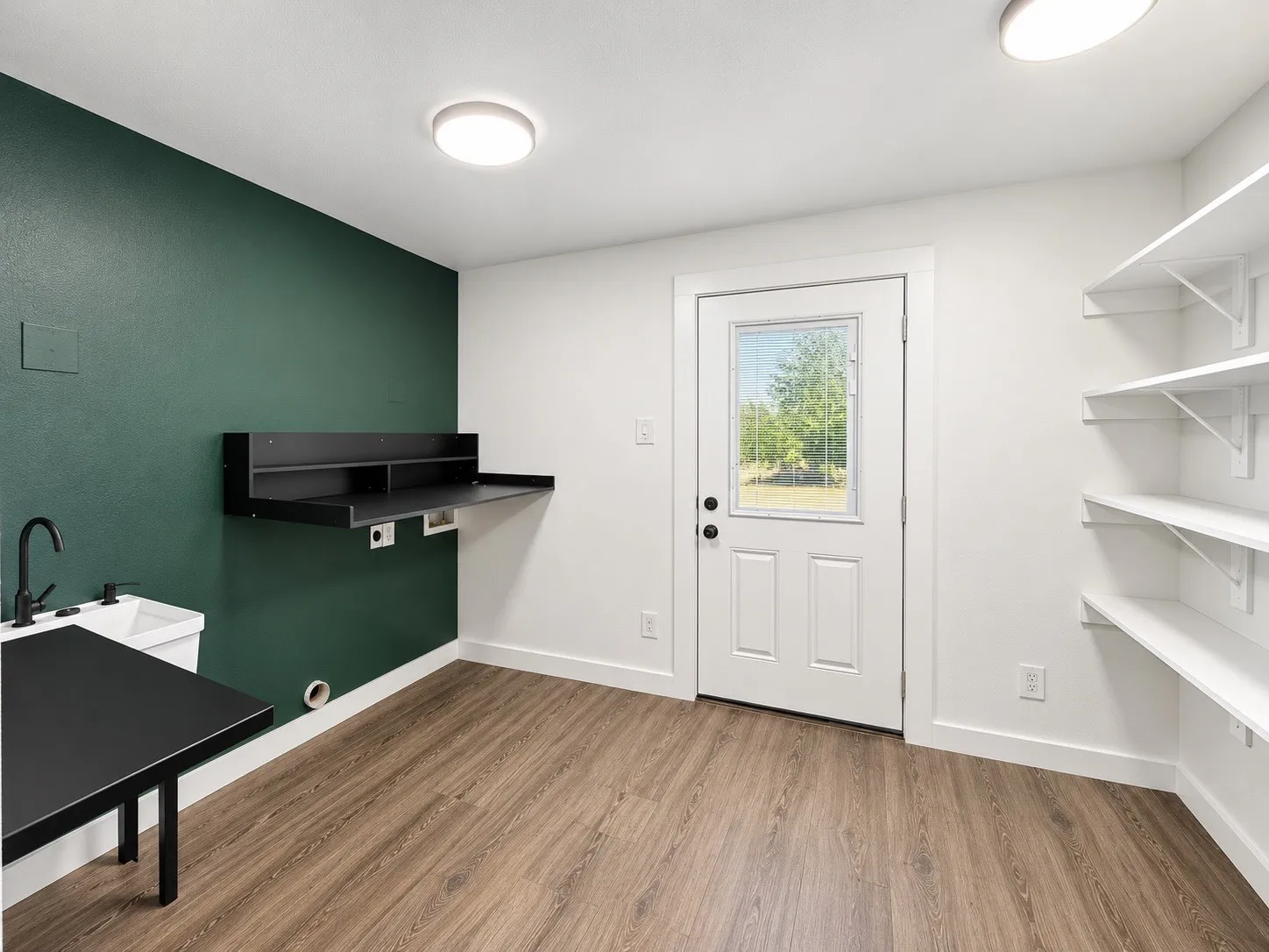 Wood-finish flooring, built-in shelving, utility sink with black faucet, and a wall-mounted desk