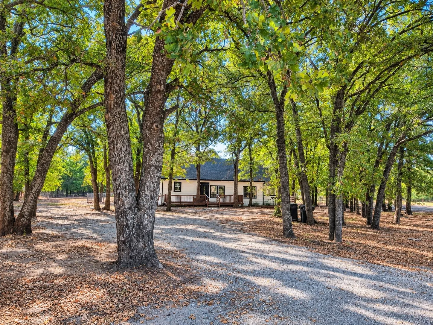 Gravel driveway leading to a white residence with a dark roof and covered porch