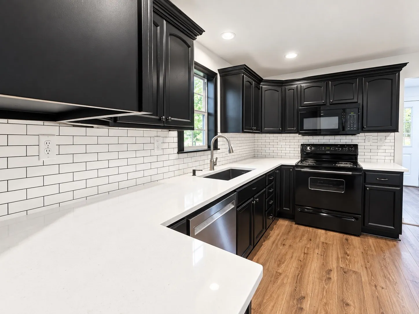 Kitchen featuring wood-finish flooring, white countertops, subway tile backsplash, and black cabinetry with crown molding