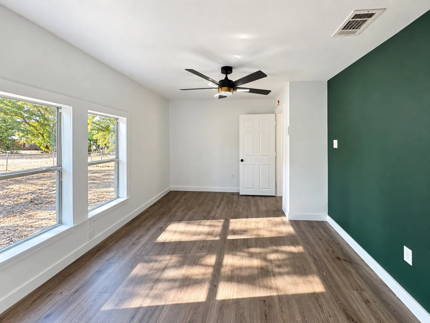 Wood-finish flooring, accent wall, ceiling fan with integrated lighting, multiple windows, and white trim
