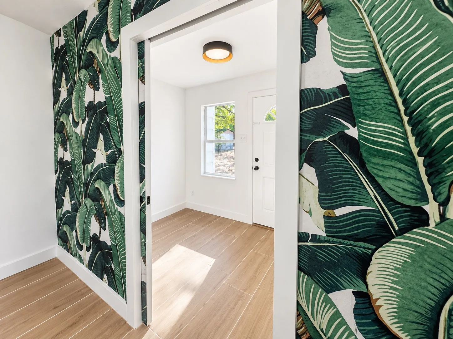 White walls with tropical print accent, wood-finish tile flooring, recessed lighting, and a white paneled door