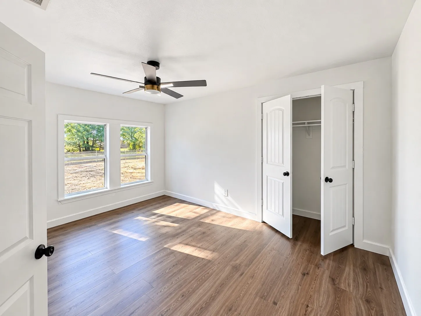 Wood-finish flooring, white walls, dual windows, ceiling fan, and a double-door closet