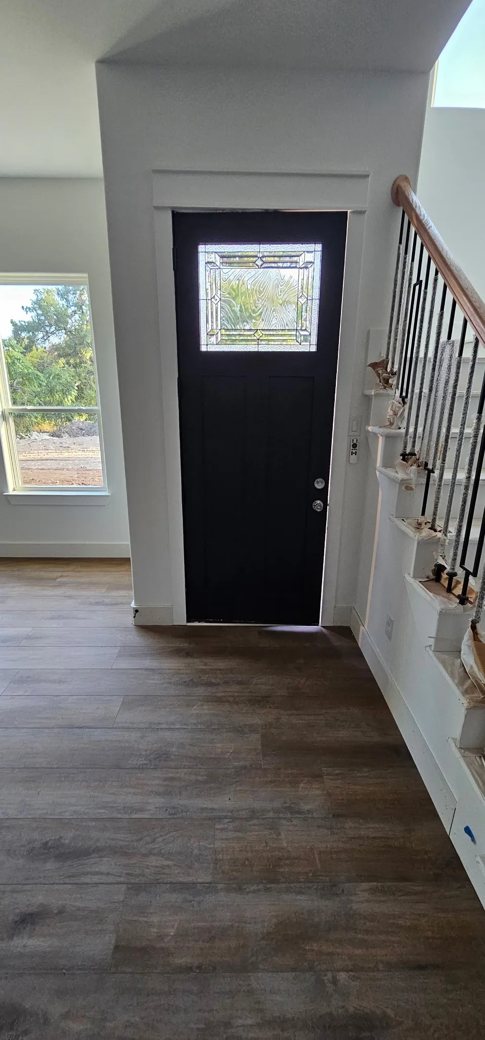 Entryway featuring a dark paneled door with leaded glass, wood-finish flooring, a white trim staircase with metal balusters, and large windows