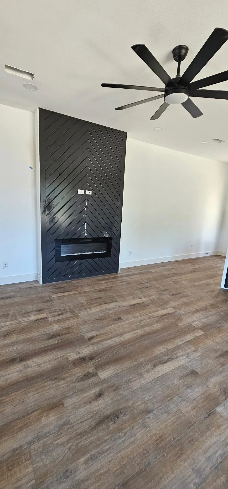 Contemporary fireplace feature wall with chevron-patterned paneling, integrated linear electric fireplace, and wood-finish flooring