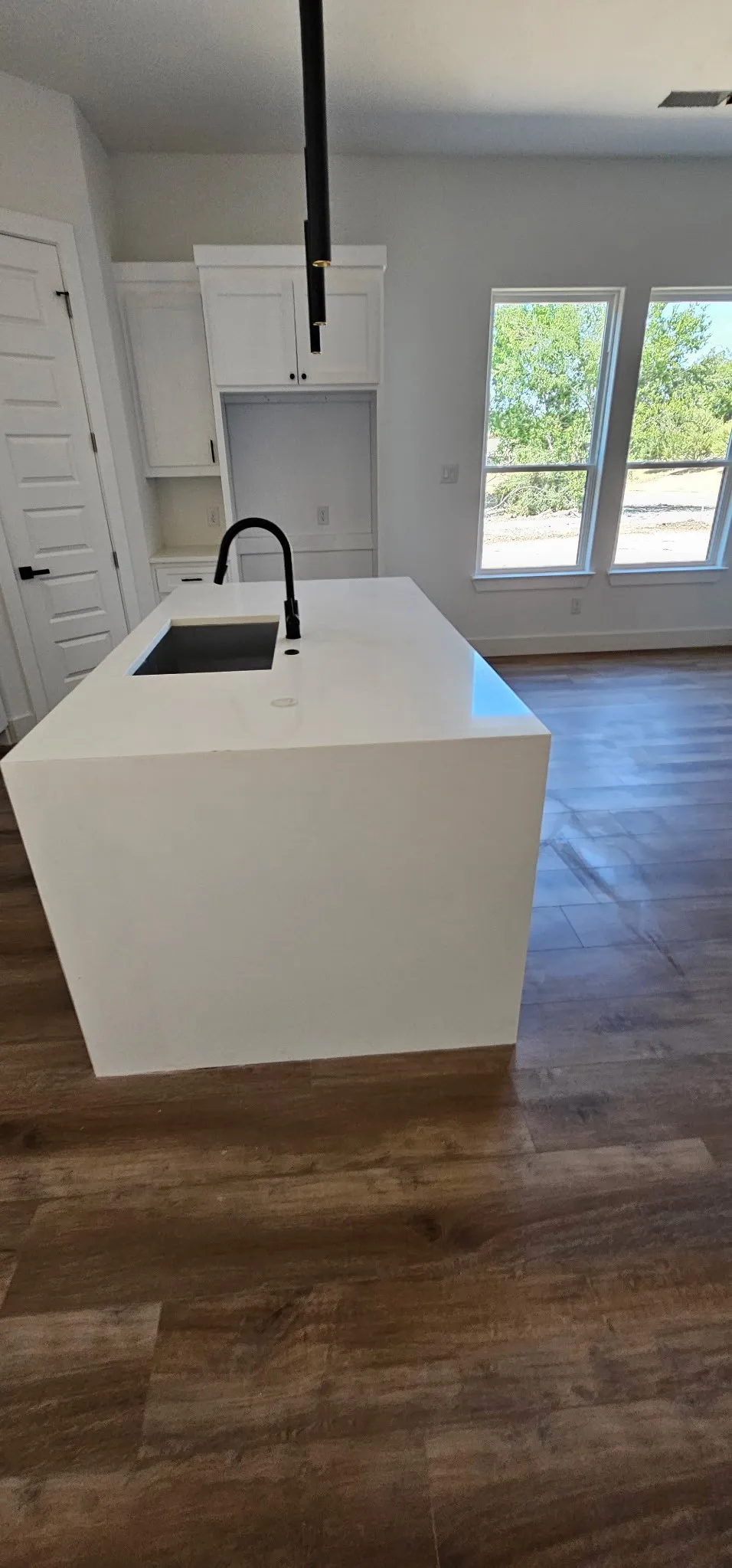 Kitchen island featuring a white countertop, an integrated sink with a matte black faucet, wood-finish flooring, white cabinetry, and multiple windows