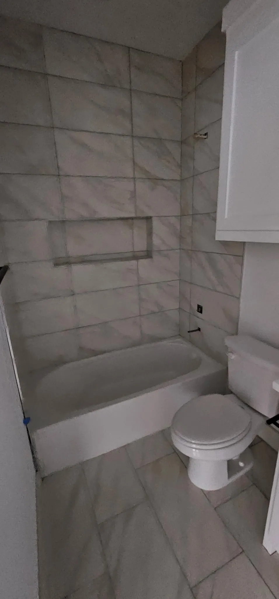 Full-height tile shower surround with an integrated niche, a white soaking tub, and tile flooring