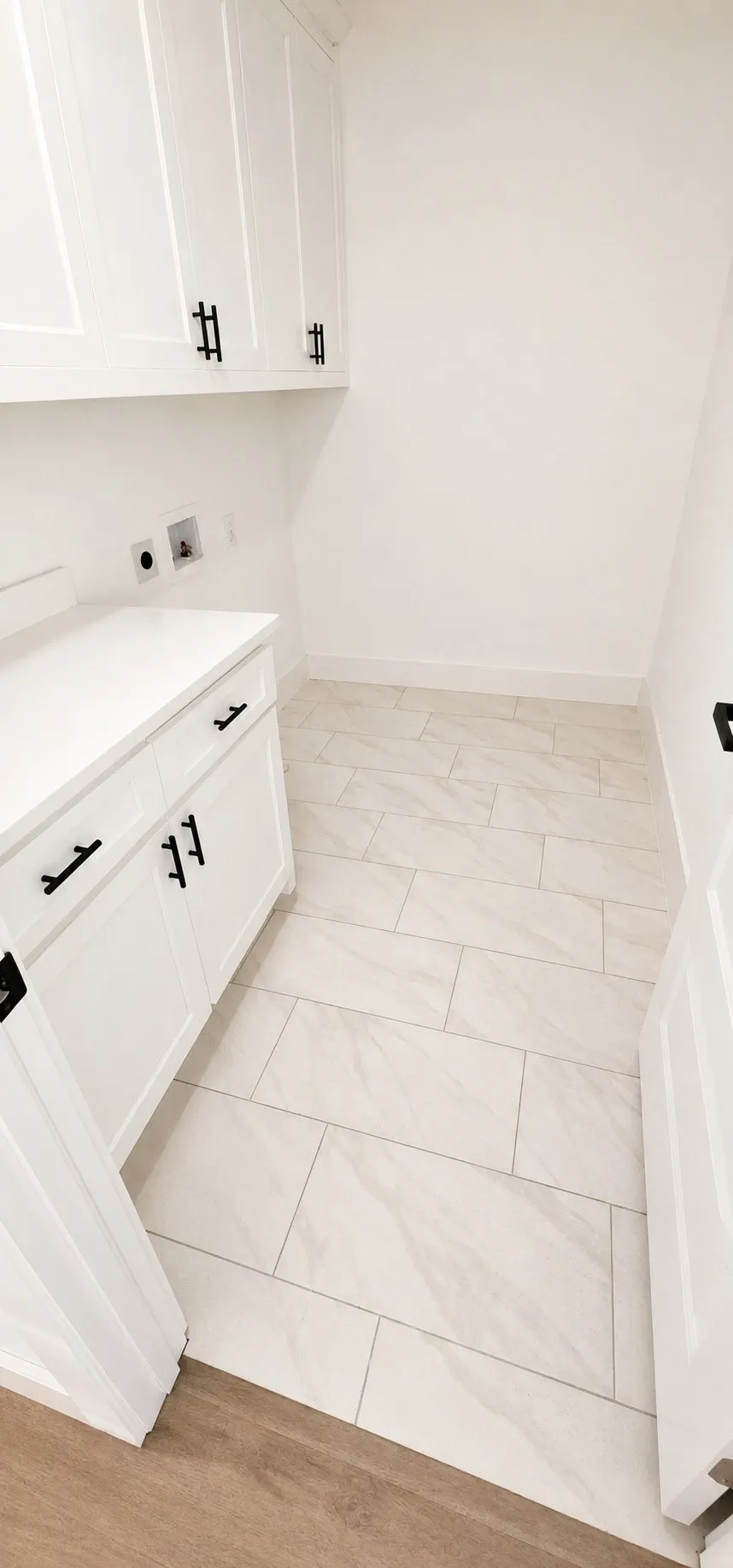 White shaker-style cabinetry with matte black hardware, solid surface countertops, and rectangular tile flooring