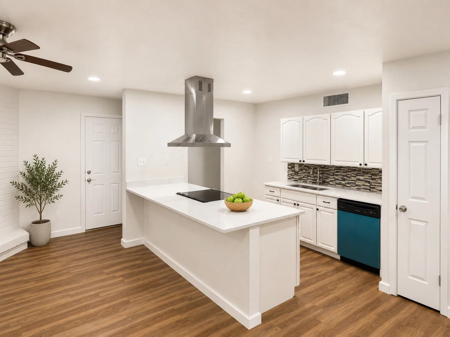 Kitchen featuring a central island with cooktop, stainless steel range hood, white cabinetry, mosaic tile backsplash, and wood-finish flooring