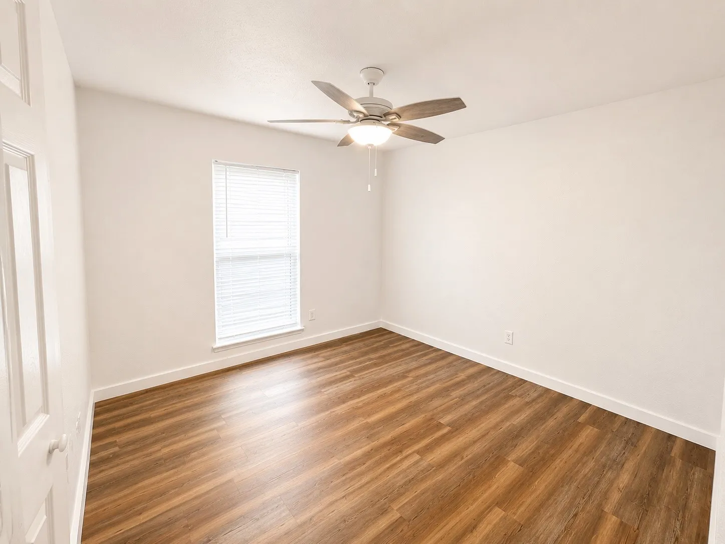 Room featuring wood-finish flooring, a ceiling fan with integrated lighting, and a window with blinds