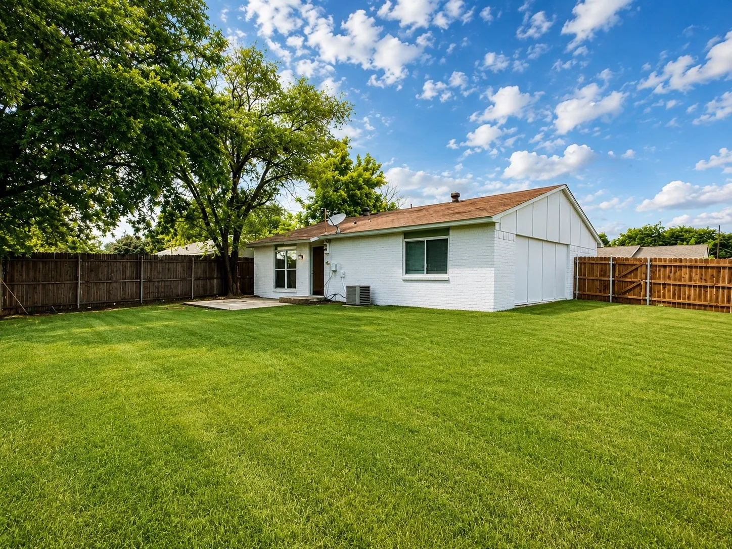 Spacious backyard featuring a large grass lawn, privacy fencing, and mature trees