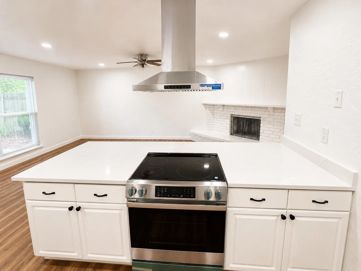 Spacious kitchen island featuring a built-in range, bright white cabinetry, and a sleek stainless steel range hood