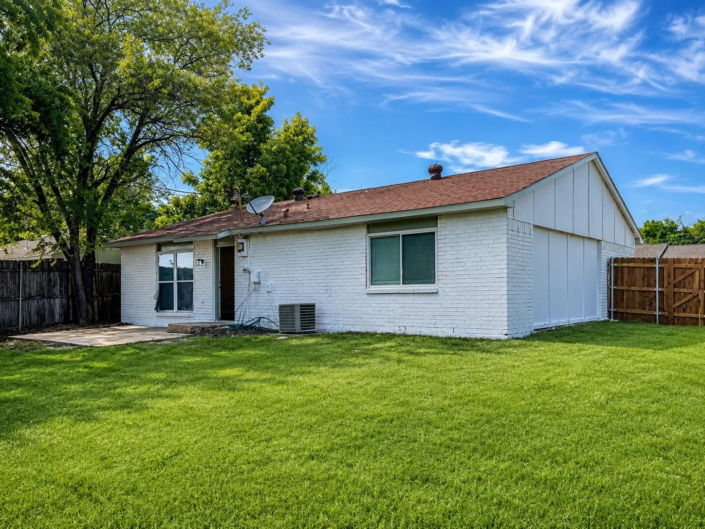 Expansive backyard featuring a manicured lawn, white brick exterior, a concrete patio, and a wood privacy fence