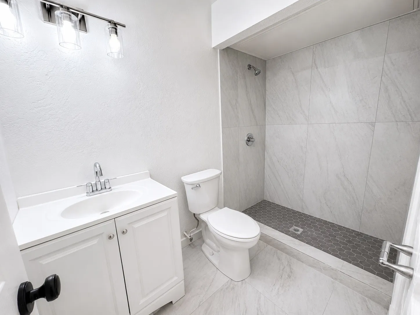 Bathroom featuring a white vanity with integrated sink, chrome faucet, and three-light vanity bar