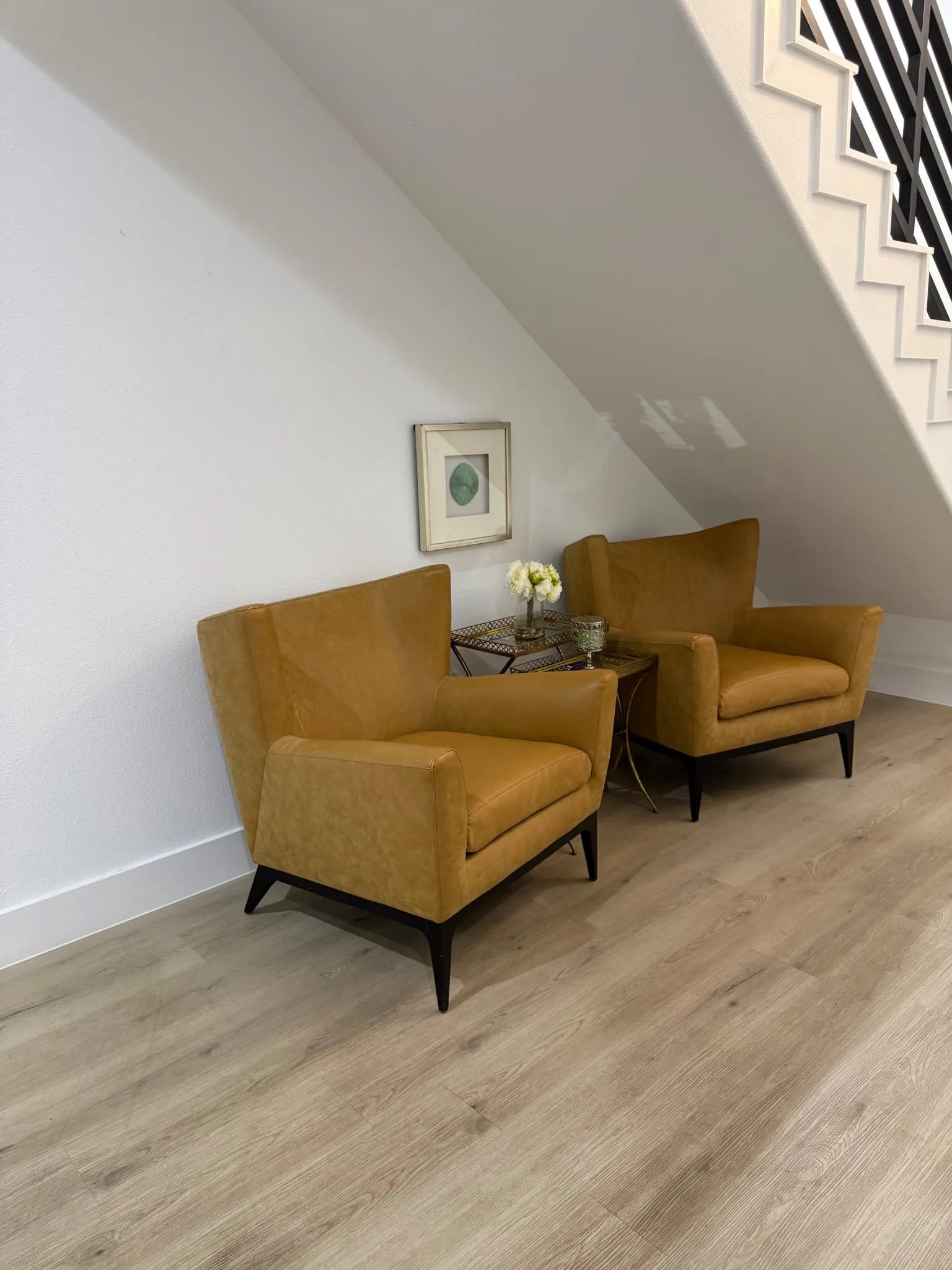 Wood-finish flooring with white baseboards, a white wall, and a staircase featuring white risers and dark balusters
